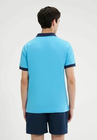 Polo di colore blu brillante con colletto e polsini blu navy. Realizzato in un tessuto liscio, presenta una vestibilità classica e maniche corte.