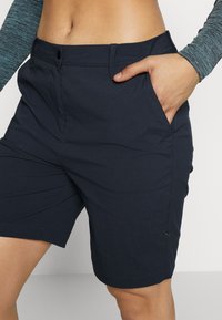 Shorts bleu marine en tissu léger, avec des poches, un devant plat et une coupe droite. La ceinture est fermée par un bouton unique.