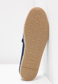 Scarpa slip-on in tessuto blu navy con suola testurizzata; presenta un motivo a zig zag per la presa e il logo TOMS incastonato sul fondo.