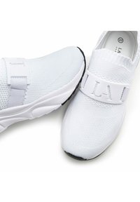 White athletic shoes with a breathable knit upper, elastic strap labeled "LA," and a textured sole. Features a black rubber accent on the toe.