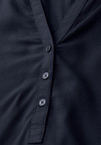 Navyblaues Hemd mit Knopfleiste aus weichem Stoff, einem Kragen und dunklen Kunststoffknöpfen entlang der vorderen Blende.