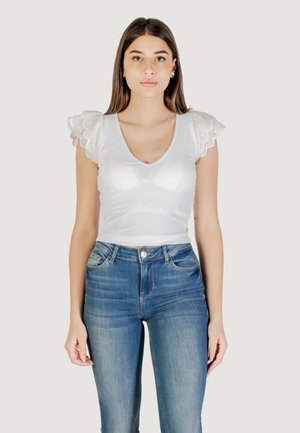 Top bianco a righe con maniche corte e dettagli in pizzo ad occhiello, abbinato a jeans blu aderenti. Il top presenta un design a scollatura a V profonda.
