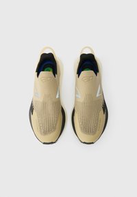 Bēšas slip-on sporta kurpes ar teksturētu adījumu, melniem akcentiem un gumijas zoli. Iezīmējas ar atstarojošiem dizaina elementiem un mērcētu apkakli.