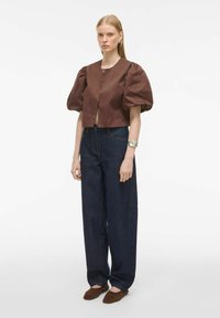 Pruun lühike pluus puffvarrukatega, kombineeritud tumedama sinise laia säärega teksade ja pruunide sandaalidega. Minimalistlik disain, ilma nähtavate mustrita.