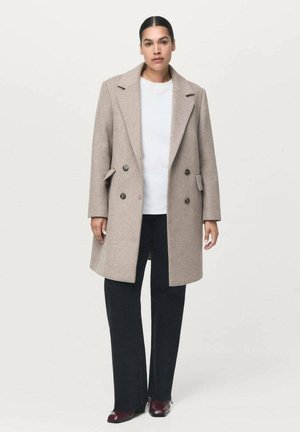 Manteau en laine beige doublé, à double boutonnage, avec de grands boutons, des poches latérales, des revers en pointe et une coupe droite, associé à un pantalon évasé noir.