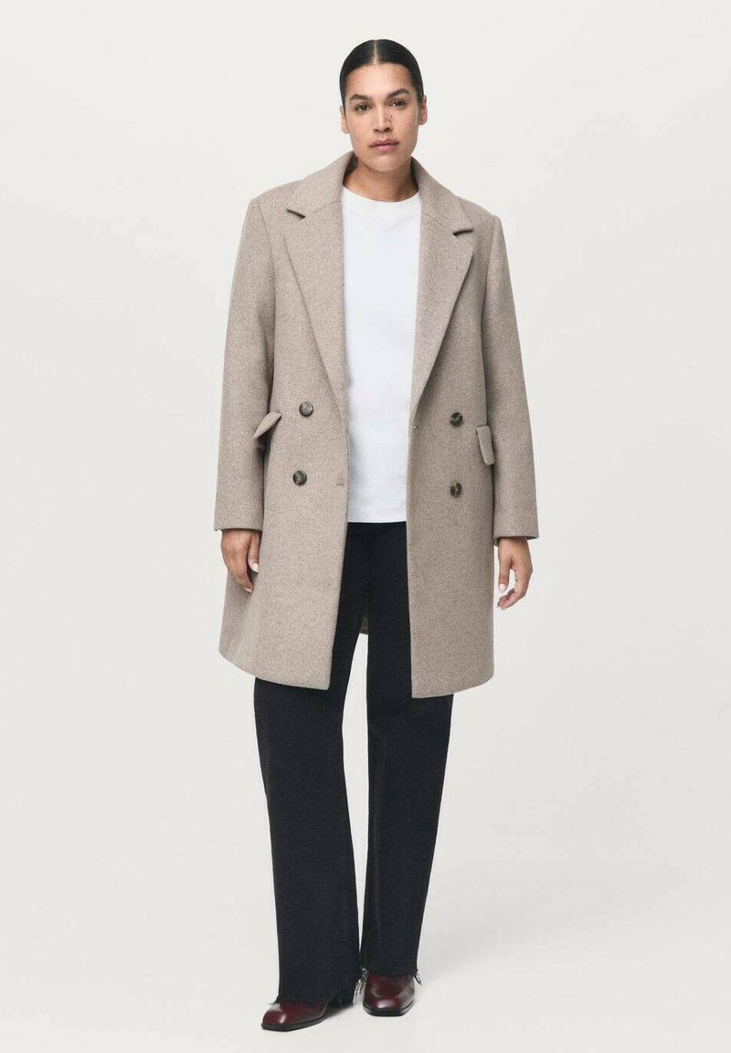 Manteau en laine beige doublé, à double boutonnage, avec de grands boutons, des poches latérales, des revers en pointe et une coupe droite, associé à un pantalon évasé noir.