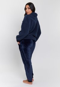 Pullover in pile di colore blu navy con collo alto e maniche lunghe; abbinato a joggers in velluto blu navy con orli a coste.