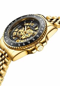 Gouden polshorloge met een zwarte bezel, skeletdiaal dat de ingewikkelde mechanica onthult, en een schakelige metalen band. Heeft Romeinse cijfers en een kroon.