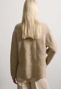 Beige gestrickter Pullover mit strukturiertem Zickzackmuster und gerippten Details. Lange Ärmel und lockere Passform.