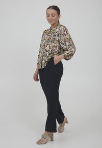Blusa floreale con maniche a sbuffo, sfondo scuro e fiori vivaci. Abbinata a pantaloni stretti blu navy e sandali con tacco a blocco beige.