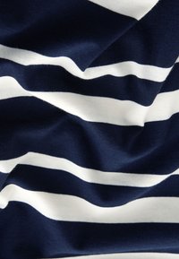 Tmavomodrá látka so širokými bielymi vodorovnými pruhmi, zobrazujúca mäkké záhyby a textúru.