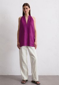Top en lin à bretelles dans un violet éclatant, avec un décolleté en V profond et une coupe ample, associé à un pantalon large blanc et des sandales noires.