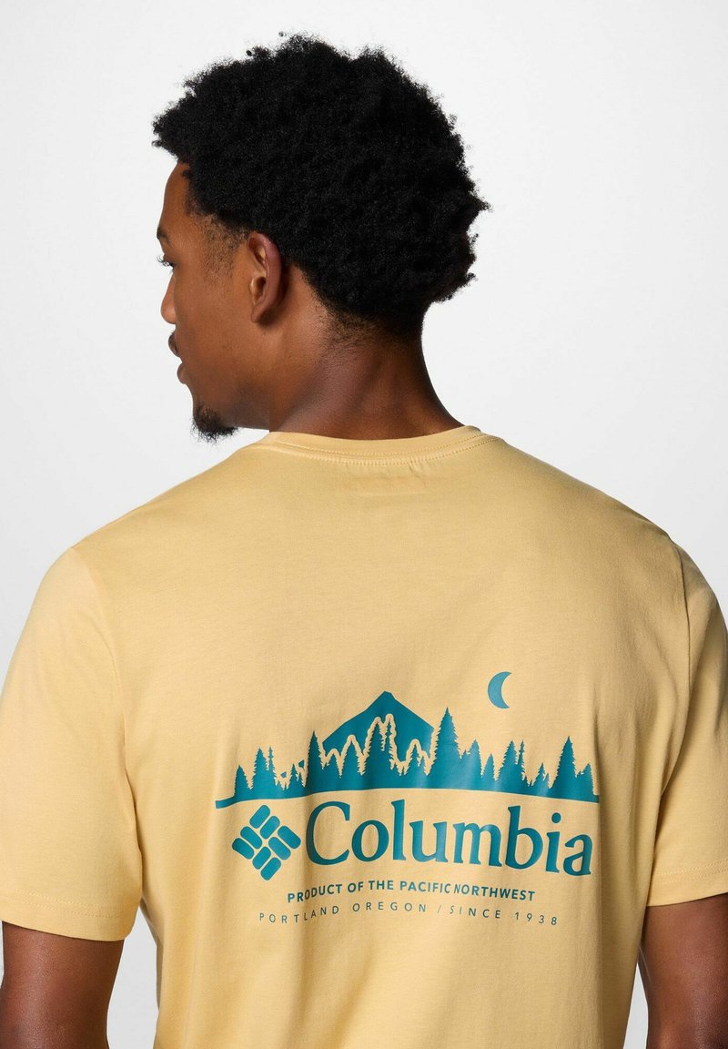 Gelbes Baumwoll-T-Shirt mit einem blauen Motiv von Bergen und Bäumen auf der Rückseite, mit dem markant dargestellten Markennamen "Columbia".