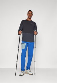 Outdoor apparel featuring a black and gray long-sleeve top, blue pants with a gray pocket, and trekking poles. Textured fabric, functional design.