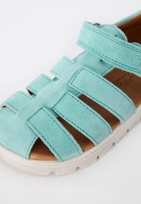 Turkos mockask sandal med flera breda remmar och en brun texturerad innersåle, med en vit gummisula och justerbar remslutning.
