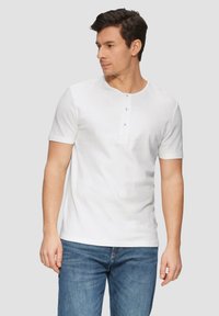Witte kortebloes met driebottonsluiting, ronde hals en gestructureerde stof, gecombineerd met blauwe denim jeans.