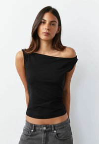 Čierny top s odhalenými ramenami z hladkej látky, priliehavý strih a krátke rukávy. Kombinovaný s vysokým pásom sivých džínsov.