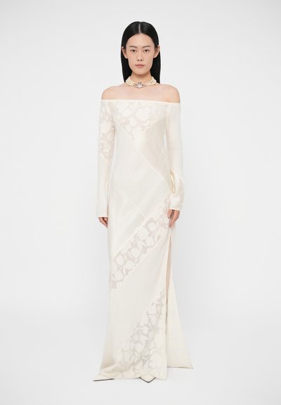 Lang off-shoulder kjole i creme med forskellige teksturer, som har blomsterprint, en sideslids og tætsiddende ærmer. Fremhævet med en halskæde.