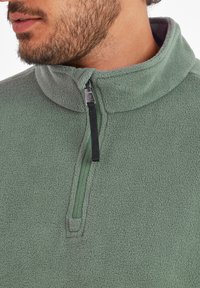 Green fleece pullover with a half-zip collar. Features include a soft texture, adjustable zipper, and reinforced stitching along the seams.