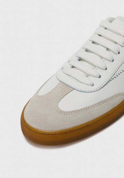 Vit sneaker med en grå tåkappa i mocka, ovandel i texturerat läder och tjock sål av gummigummi med platta vita snören.