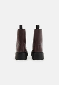Botas de tornozelo bordeaux com parte superior em couro liso, bico redondo e sola de borracha preta. Apresenta puxadores e uma marcação mínima de lado.