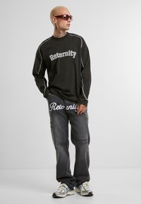 Mustikas pikkade varrukatega särk, millel on "Reternity" tekst, hallad püksid, kerged kulumisjäljed ja "Reternity" trükk. Hõbedane aksessuaaridest kett ja tennisetossud.