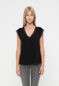Top nero con scollatura a V e maniche corte a cappuccio. Un profilo in pizzo lungo il collo e i bordi delle maniche aggiunge texture e dettagli. Design semplice e aderente.