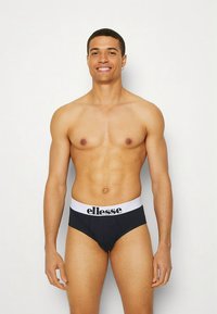 Zwarte slip met een witte tailleband met het "ellesse"-logo. De stof lijkt glad en rekbaar, gevormd voor pasvorm en comfort.