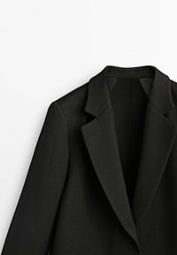 Blazer noir avec un col cranté, des épaules structurées et une texture lisse. La doublure intérieure est noire, avec un design minimaliste.