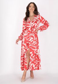 Rochie maxi roșie cu un model unduit alb, mâneci lungi, decolteu în V, talie strânsă și o fentață frontală. Material ușor cu un design fluid.