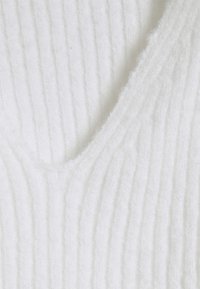 Weißes Strickoberteil mit einem strukturierten Rippendesign, V-Ausschnitt und weichem, flauschigem Material mit sichtbaren Nähdetails.