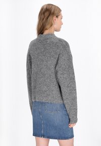Pulover scurt gri cu finisaj texturat, guler rotund și mâneci lungi, asortat cu o fustă din denim albastru cu buzunare la spate.