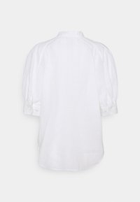 Blouse blanche à manches longues avec manches bouffantes, poignets boutonnés et ourlet arrondi, vue de dos sur un fond uni.