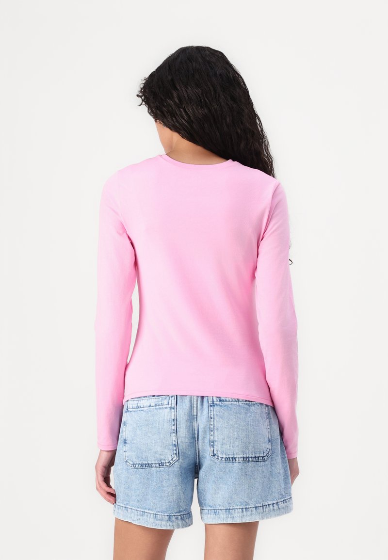 Langärmliges pinkes T-Shirt aus weichem Material, mit rundem Ausschnitt, taillierter Passform und lässiger Rückenansicht, kombiniert mit hellen Jeansshorts.