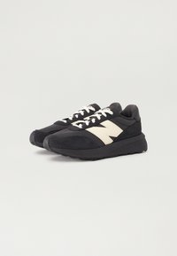 Chaussures de sport noires avec une tige en maille et des accents en daim, dotées de lacets blancs et d'une semelle en caoutchouc noir texturé. Design de logo beige distinctif.