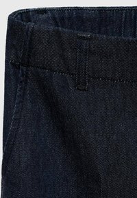 Tamno plava trapernina s suptilnom teksturom. Ima pojas i detalje šivanja, prikazujući klasičan dizajn traperica.