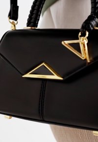 Borsa a tracolla in pelle nera con un accento dorato triangolare e chiusura, dotata di manico intrecciato e forma strutturata. Corpo testurizzato con linee pulite.