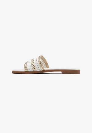 Sandalo flat con cinturino intrecciato bianco e oro e suola marrone, mostrato di profilo su sfondo bianco.