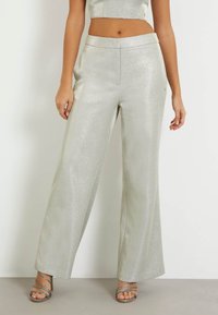 Pantalons larges argentés en tissu brillant et texturé. Dotés d'une taille lisse et de poches sur les côtés. Associés à des sandales à talons métalliques.