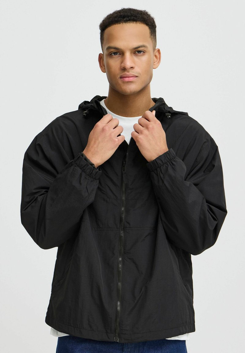 Veste noire légère avec fermeture éclair à l'avant, capuche, poignets élastiques et coupe décontractée. Fabriquée en tissu lisse et durable.