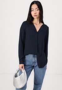 Marinebluse med v-hals, lange ermer og avslappet passform, parret med lyseblå høytidelte jeans og en sølvfarget lærveske.