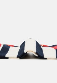 Navy- und cremefarbener gestreifter Stoff mit roten Akzenten. Weiche Textur mit sichtbaren Nähten und einem gefalteten Design.