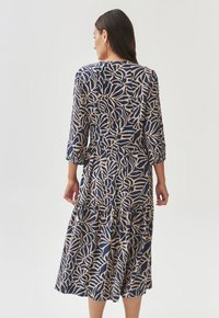 Vestido de estampado floral con base azul marino, patrones de hojas beige, mangas tres cuartos y dobladillo con volantes, hecho de tela ligera.