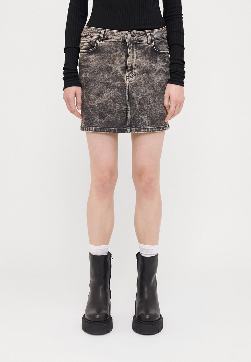 Femme portant un haut côtelé noir à manches longues, une mini-jupe en denim noire à motif étoiles, des chaussettes blanches et des bottines en cuir noir épaisses.