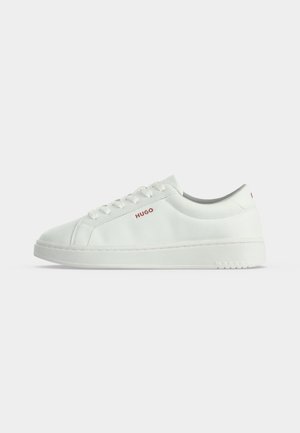 Baskets basses blanches avec lacets et logo rouge "HUGO" sur le côté, sur un fond blanc uni.