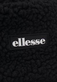 Black, fluffy fabric with a textured surface; features a rectangular black label with white "ellesse" branding.