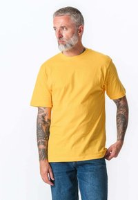 Gul kortærmet T-shirt i bomuld med rund hals og afslappet pasform, iført med blå denim jeans.