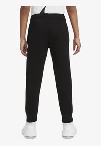 Pantalones de chándal negros con una cintura elástica, tobillos ajustados y una textura suave, combinados con zapatillas blancas.