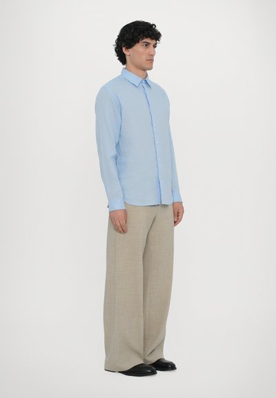 Chemise à manches longues bleu clair avec un devant à boutons, assortie à un pantalon large beige texturé et des chaussures noires.