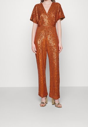 Woman wearing a sleeveless, copper-orange, sequined jumpsuit with a V-neck and wide-leg pants, paired with gold high-heeled sandals.